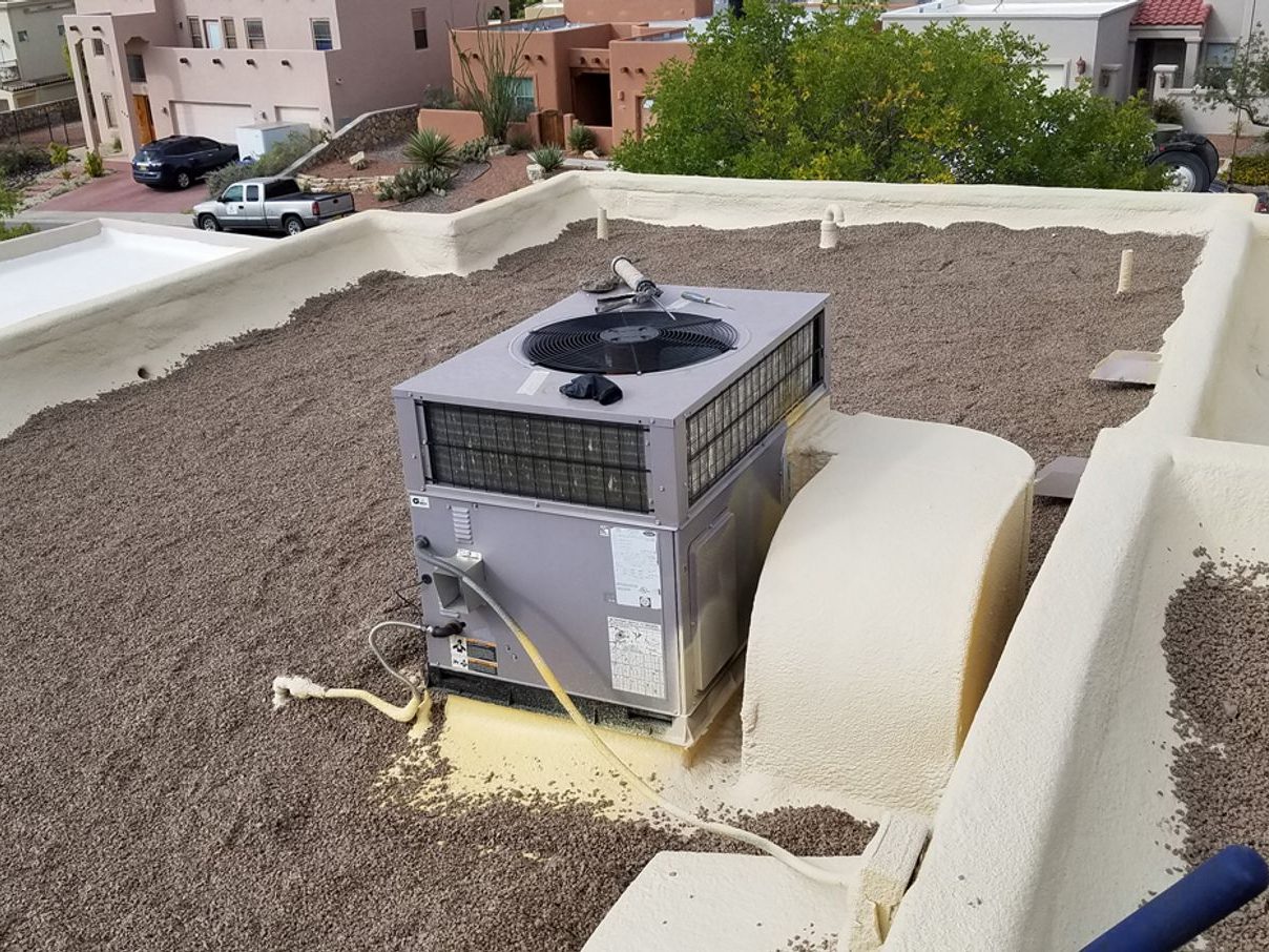 Completed spray foam roof on a commercial building with a rooftop unit foamed and coated around its base