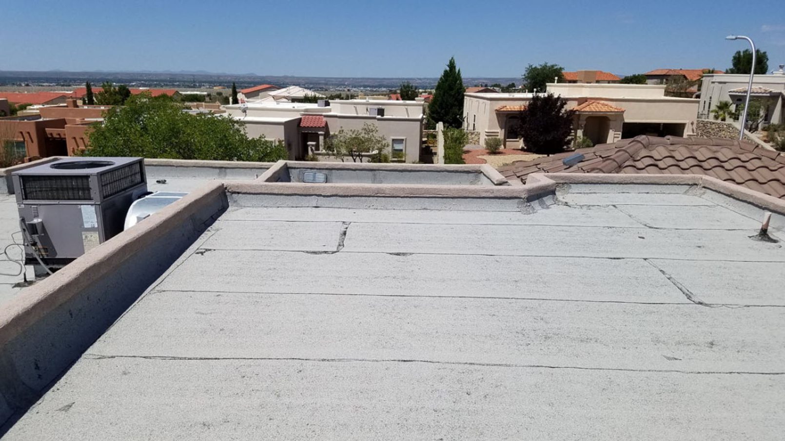 Seamless spray foam roof running unbroken to the parapet walls on a flat Albuquerque roof, with rooftop equipment coated at the base