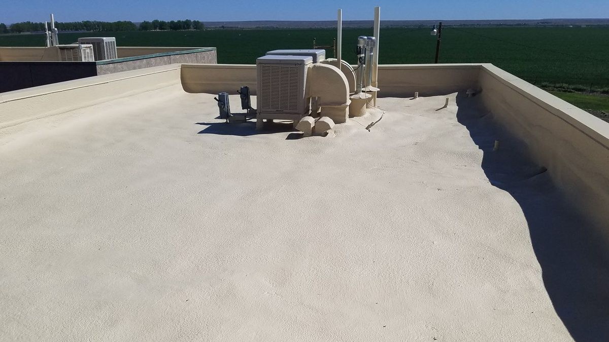 Seamless spray foam roof running unbroken to the parapet walls, with rooftop units and ductwork foamed and coated at the base